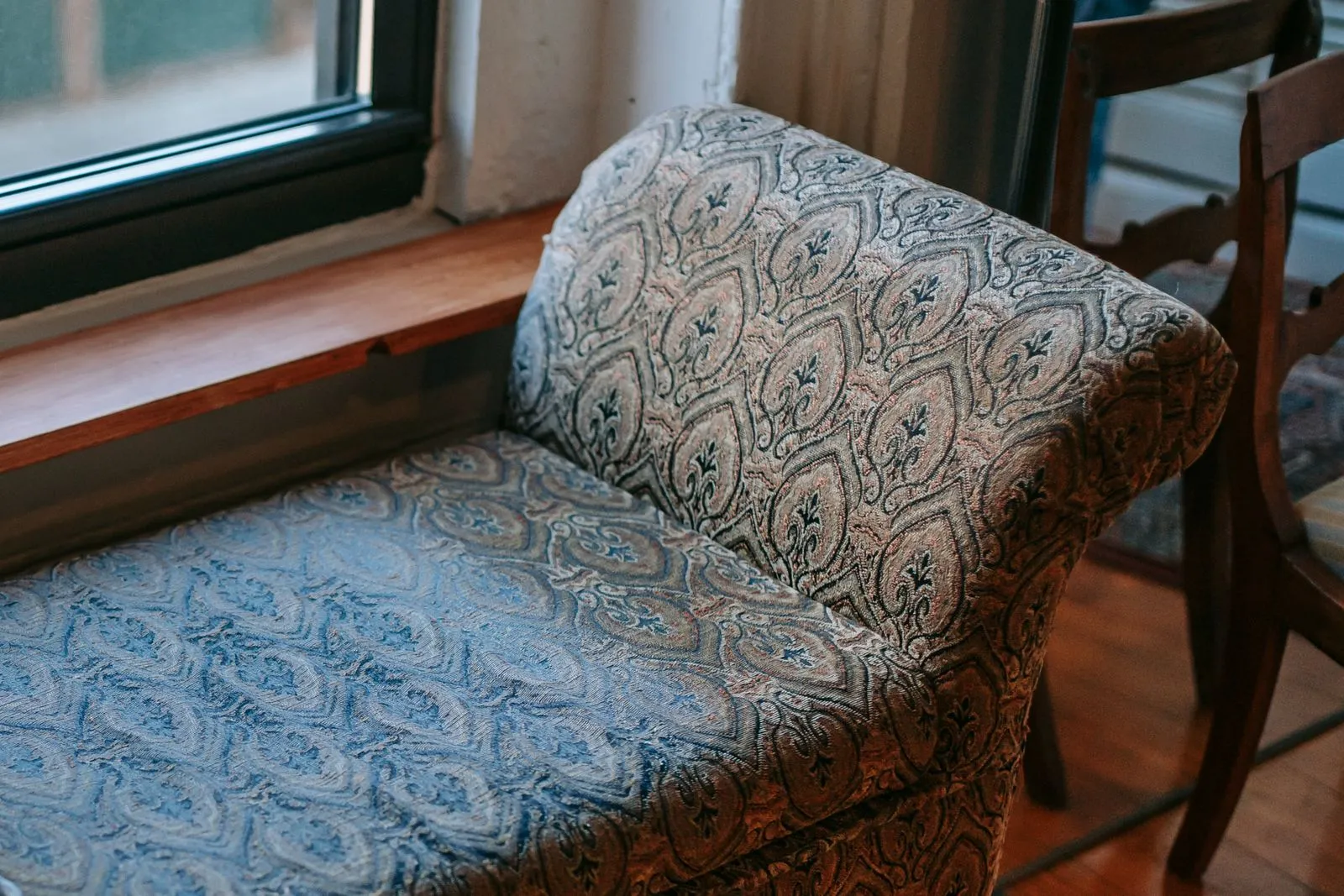 From above of comfortable elegant ottoman bench placed on parquet floor near window in cozy apartment